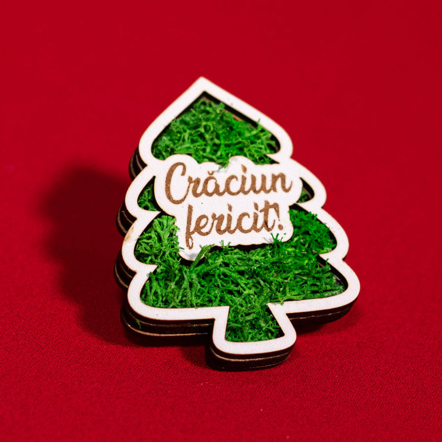 Magnet decorativ din lemn în formă de brad, cu licheni verzi și mesajul ‘Crăciun fericit’.